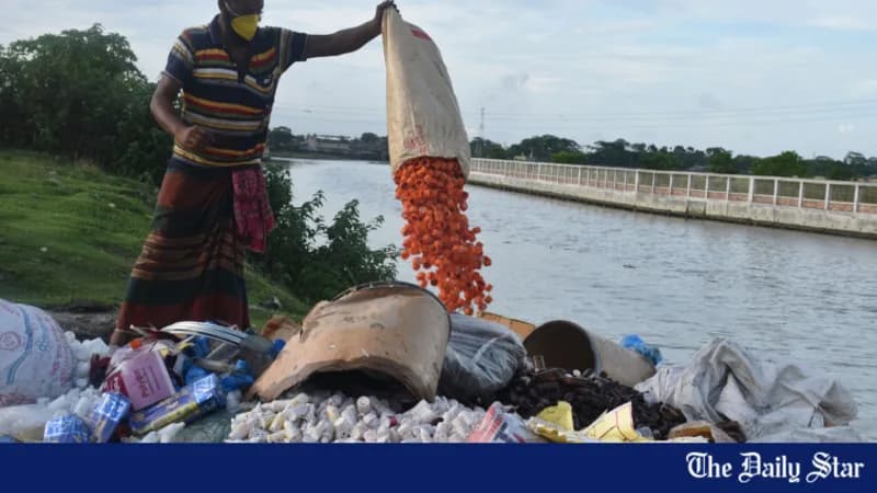 A worker tipping a drum of confiscated medicine and cosmetics onto a heap beside a river.